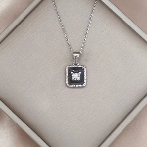 Detail eines Vintage-Quadrat-Anhängers mit Silber-Schmetterling auf schwarzem Emaille