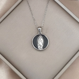 Nahaufnahme der silbernen Jungfrau Maria Guadalupe Kette auf einem Seidenhintergrund