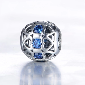 Detail van een S925 zilveren bedel met opengewerkte harten en drie blauwe edelstenen
