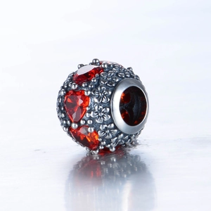 Détail macro de la perle en argent S925 avec motifs floraux et zircon de cœur rouge