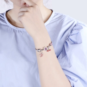 Detail of silver snake chain bracelet with purple flower and red cherry charms on wrist