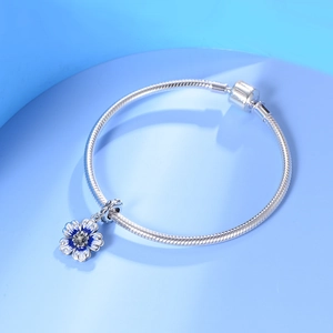 Macro detail of silver snake chain bracelet with blue and white enamel floral charm