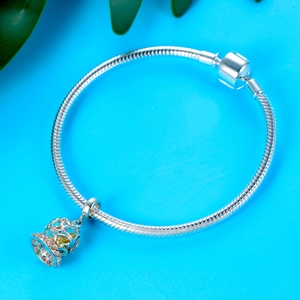 Detail of silver snake chain bracelet with hollow cage charm and pink gemstones