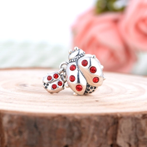Detailed view of S925 silver ladybug charm featuring red crystals on a wooden base