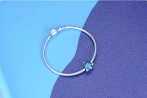 Detail of silver snake chain bracelet featuring a blue fish charm with sea blue enamel