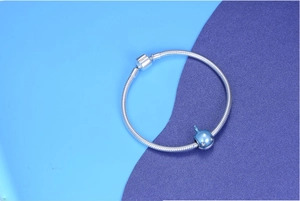 Macro detail of silver snake chain bracelet with blue whale charm and crystal accents