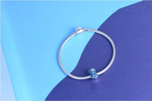 Detail of silver snake chain bracelet featuring a blue enamel charm with floral patterns