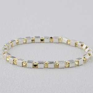 Macro shot of silver cube beads and gold faceted round beads on an elastic bracelet