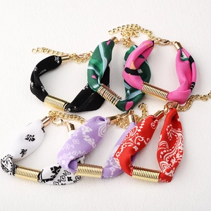 Detalle de pulseras de pañuelo de seda con estampado paisley y acabados metálicos dorados