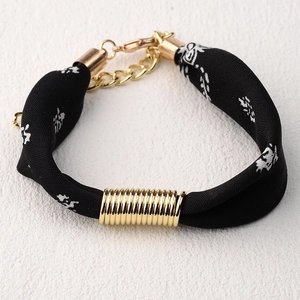 Detalle de una pulsera de seda trenzada negra con anillos dorados y cierre de mosquetón