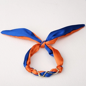 Detalle de diadema de satén azul y naranja con cadena dorada y diseño de lazo chic