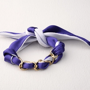 Detalle de la pulsera de pañuelo de seda morada y blanca tejida con cadena de metal dorado