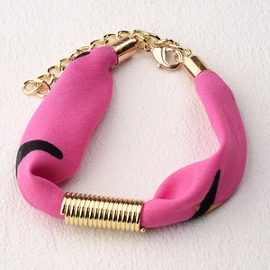 Vista macro de pulsera de tela rosa con detalles de espiral dorada y cierre de mosquetón