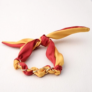 Detalle de pulsera de seda roja y amarilla con cadena dorada y un lazo de diseño elegante