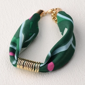 Detalle de una pulsera de tela con motivo floral verde oscuro y anillos de metal dorado