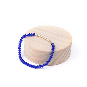 Détail de perles de cristal bleu marine facettées et tube en métal doré sur bois
