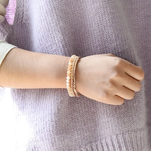 Détail de perles en or rose et de bracelets en pierre naturelle rose sur un modèle