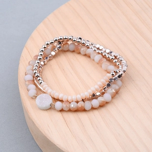 Détail d'un bracelet extensible multicouche avec perles or rose et cristaux sur du bois
