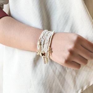 Detail of layered white bead bracelet with gold moon and butterfly charms on a model