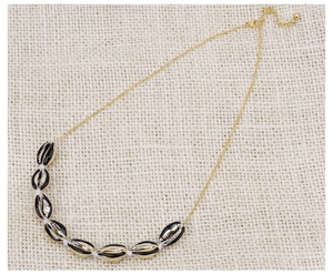 Dettaglio di collana bohémien dorata con ciondoli a conchiglia nero e oro su tessuto di lino