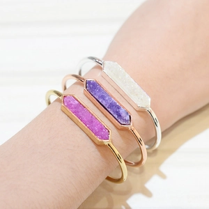 Dettaglio di tre bracciali rigidi aperti in metallo con pietre druzy esagonali colorate