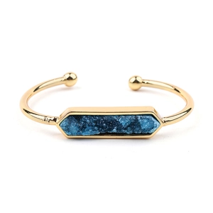 Dettaglio ravvicinato di un bracciale rigido dorato con pietra Druzy blu esagonale