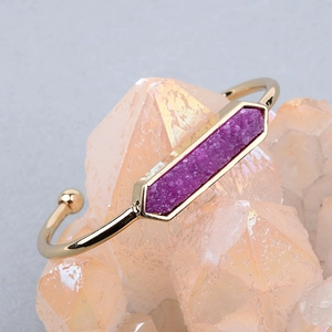 Dettaglio macro di un bracciale rigido dorato regolabile con pietra druzy esagonale viola