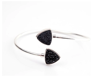 Detalle de brazalete plateado con incrustaciones de piedra negra sobre un fondo blanco