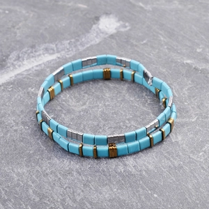 Close-up of bohemian blue and gold Tila bead bracelets on a dark stone surface