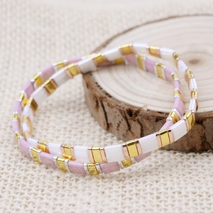 Macro detail of handmade Tila bead bracelet with pink, cream, and gold beads on wood