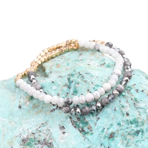 Dettaglio di braccialetti elastici in pietra naturale e perline acriliche dorate su roccia blu
