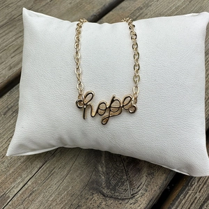 Golden Rolo chain necklace with hope script pendant on a white jewelry cushion