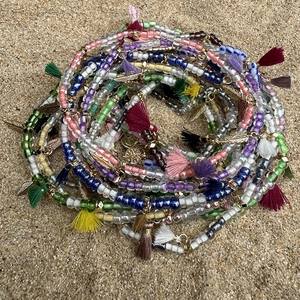 Detalle de tobillera bohemia de cuentas con borlas de colores y colgantes de hoja sobre arena