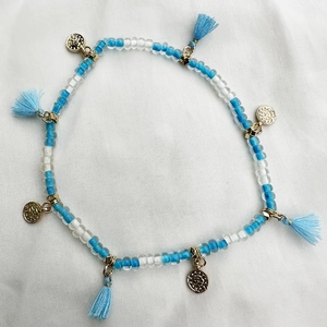 Detalle de la tobillera bohemia de cuentas con dijes dorados y borla de seda azul