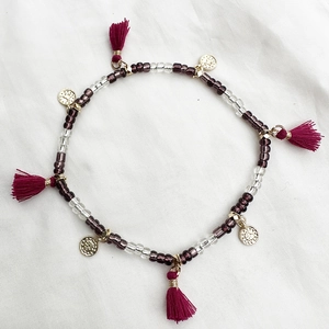 Detalle de tobillera bohemia con cuentas púrpuras, monedas de oro y borlas rojo vino