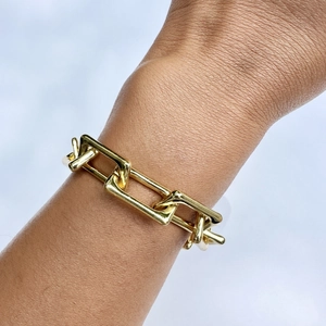 Nahaufnahme eines klobigen goldenen Gliederkettenarmbands am Handgelenk einer Frau