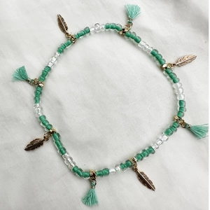 Detalle de tobillera bohemia de cuentas con colgante de pluma dorada y borlas verde menta