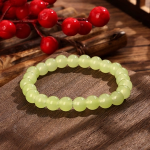 Detailed view of pale green round beads bracelet on dark wood with red berries accent