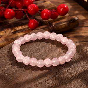 Polished light pink rose quartz beaded bracelet displayed on a rustic wood background
