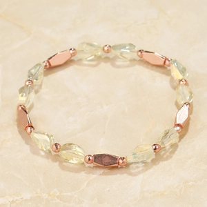 Close-up of yellow beaded bracelet with rose gold metal accents on marble texture