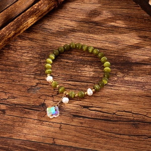 Detail of beaded bracelet with green cat-eye stones, baroque pearls and clover pendant