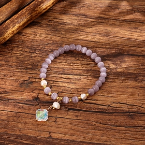 Macro shot of purple cat eye stone beads, freshwater pearls, and clover charm on wood