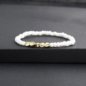 Bracelet artisanal avec perles blanches rondes et accents dorés sur fond de pierre