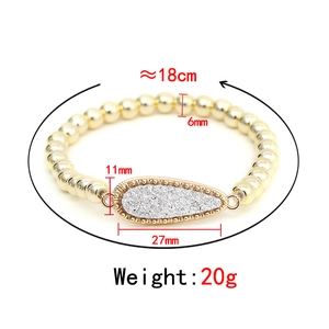 Golden beaded elastic bracelet with a sparkling teardrop pendant on a white background