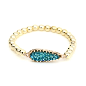 Detail of golden beaded bracelet featuring a teardrop-shaped teal druzy stone setting