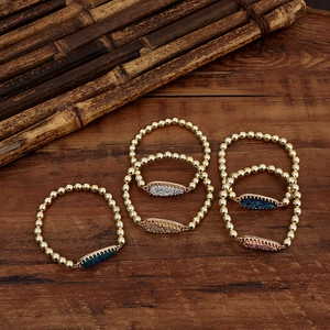 Golden bead bracelets with teardrop crystal charms in various colors on wooden surface