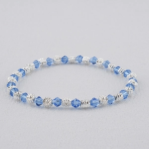 Détail de perles en cristal bleu foncé et de breloques fleurs argentées sur un bracelet