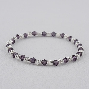 Gros plan de perles en cristal violet foncé et breloques de fleurs en argent sur un bracelet
