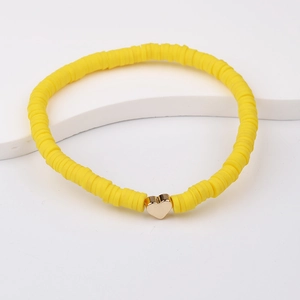 Detail of yellow polymer clay bead bracelet with a gold heart charm on a white stand