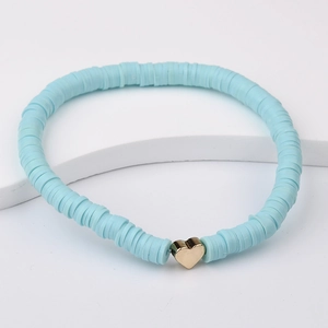 Close-up of light blue Heishi clay bead bracelet with a gold heart charm on a white stand